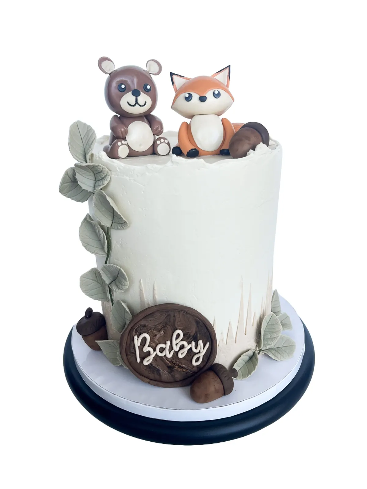 White celebration cake with woodland animal toppers and sage leaves