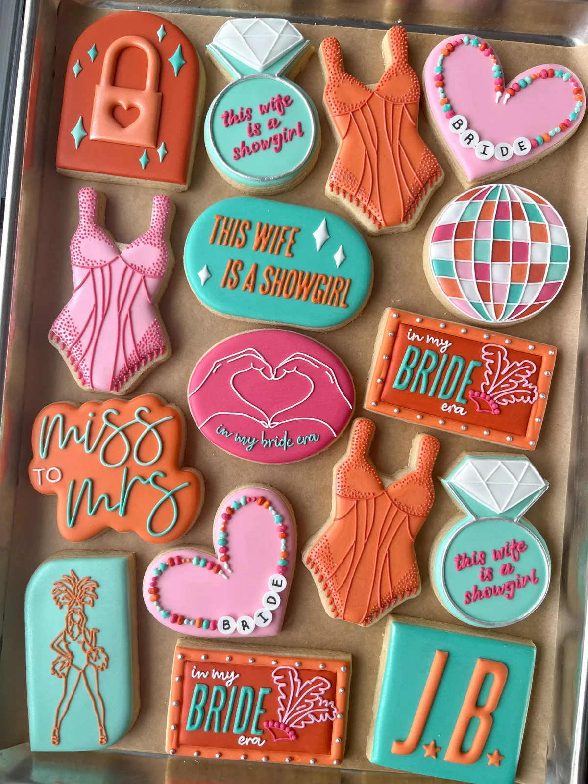 A tray of bachelorette cookies iced in coral, teal and pink: hearts, dresses, a disco ball and a bride sign